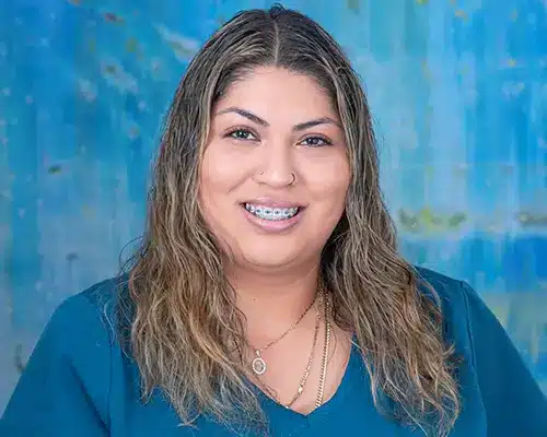 Rosa Molinero_img Professional headshot of smiling woman with long brown hair against blue background for orthodontics practice.